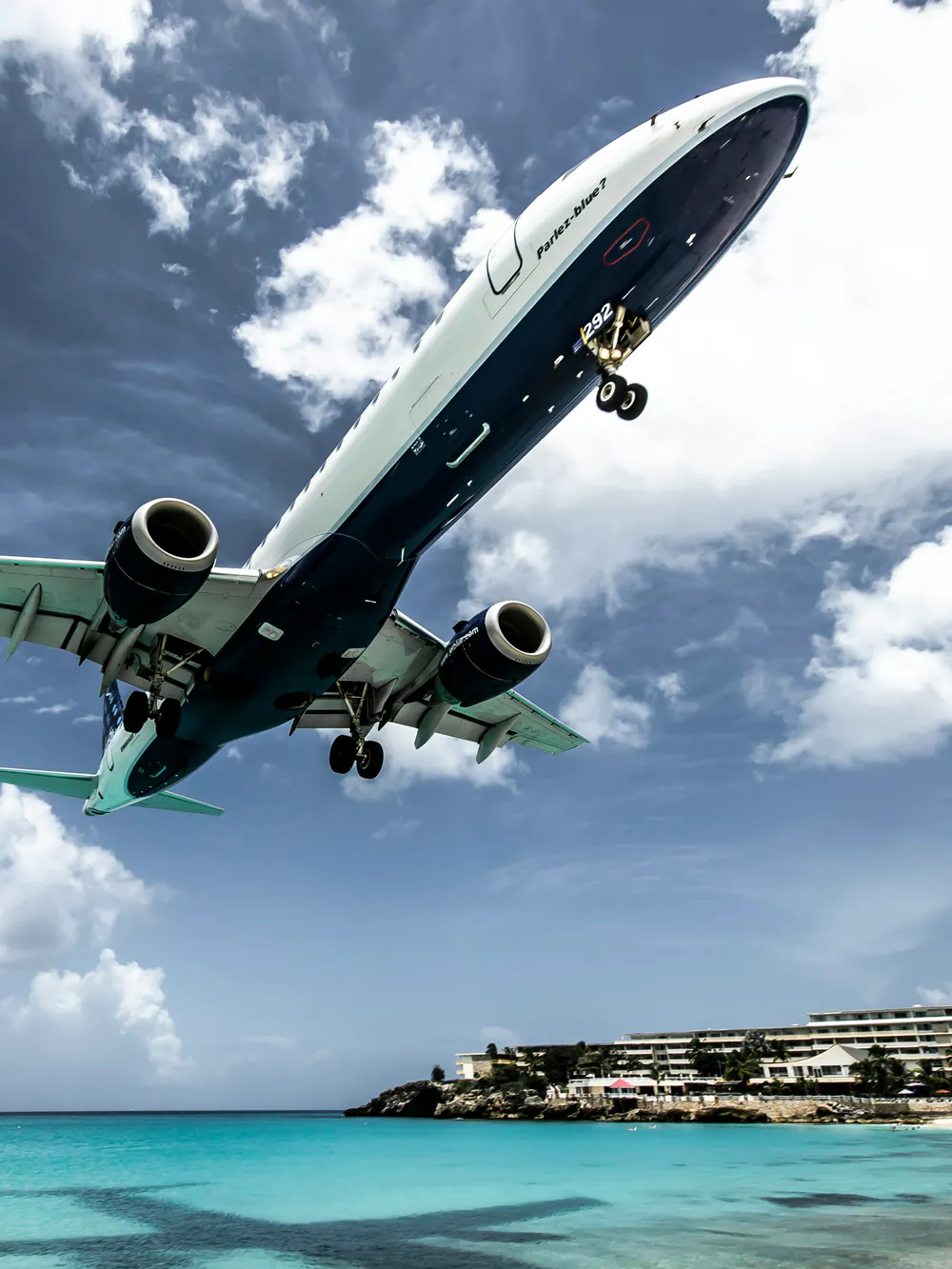 A passenger jet coming in low over turquoise water and a beach